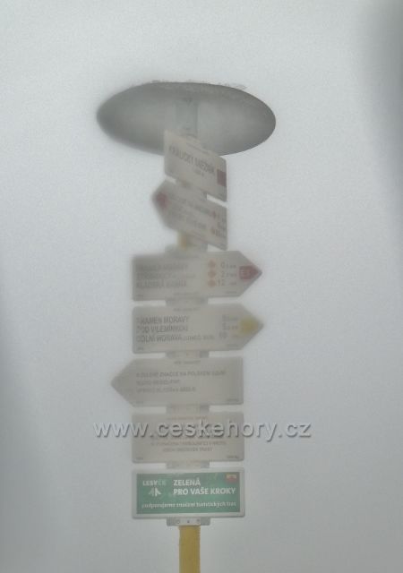 Turistický rozcestník "Králický Sněžník 1424 m.n.m." na vrcholku hory je zahalen mlhou