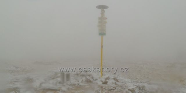 Turistický rozcestník na vrcholu Králického Sněžníku vystupuje z mlhy
