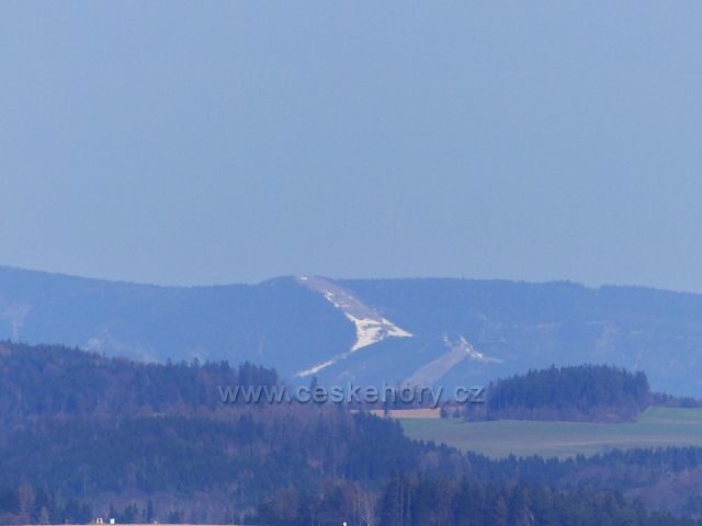 Dlouhoňovice - pohled z okraje lesa nad sjezdovkou pomocí zoomu na Slamník a Stezku v oblacích v masivu Králického Sněžníku
